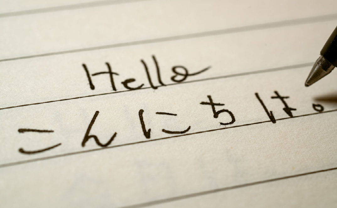 a sheet of paper shows the word "hello" written above Japanese characters that read "konnichiwa"