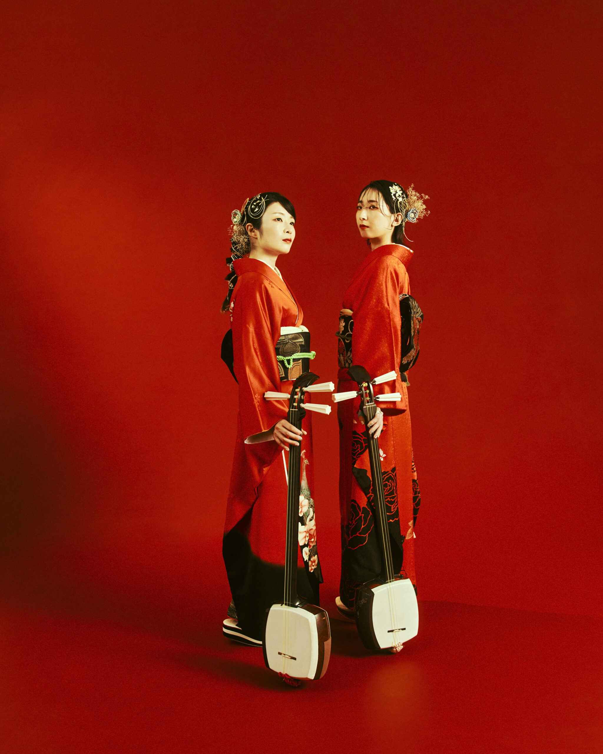 the two members of KiKi stand in red kimono against a red background