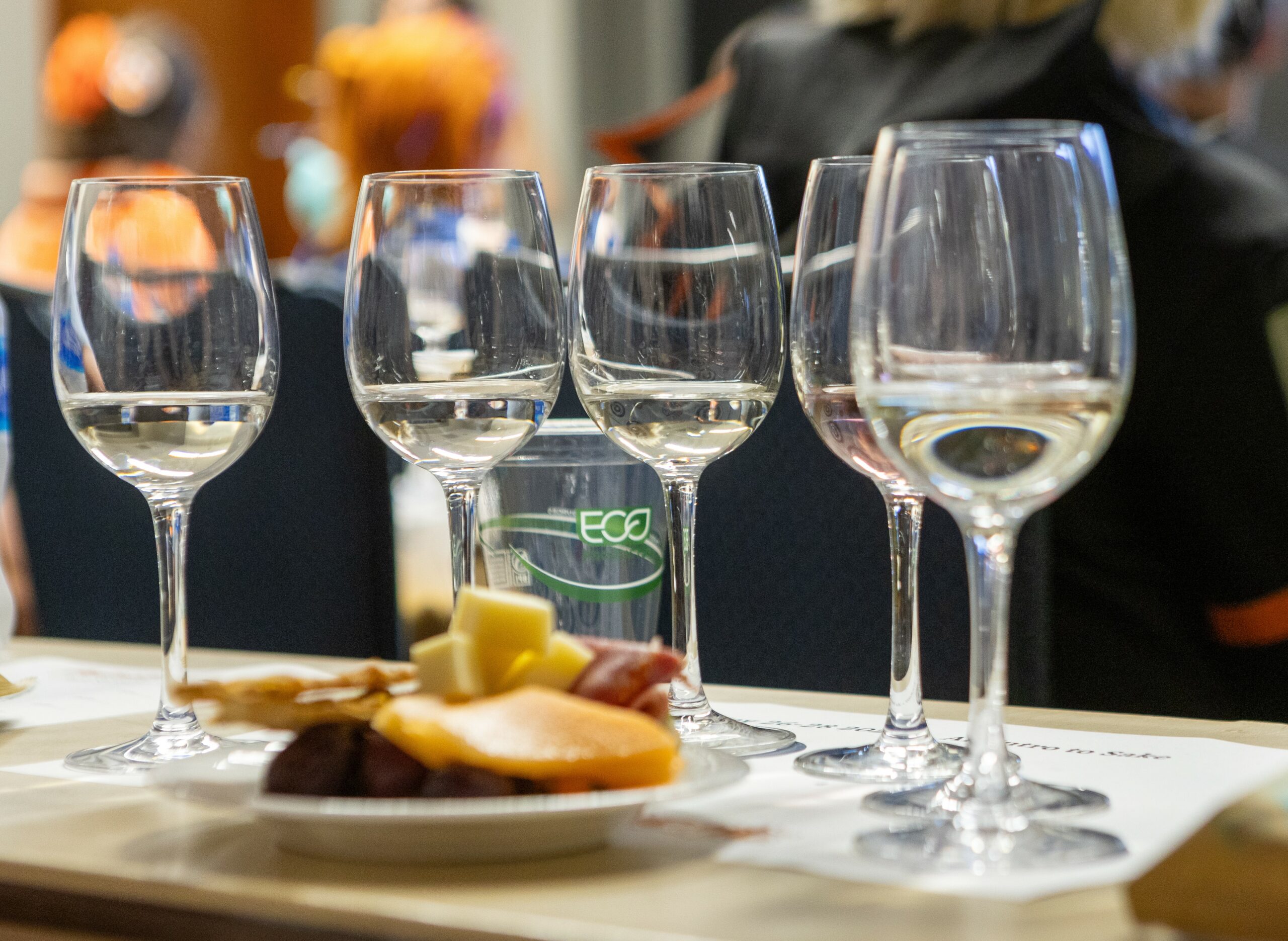 five wine glasses sitting on a table. each glass contains a tasting portion of sake. a plate of snacks sits in front of the glasses